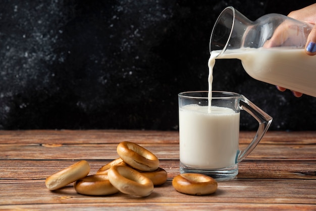 Mujer vertiendo leche en el vaso y galletas redondas sobre mesa de madera.