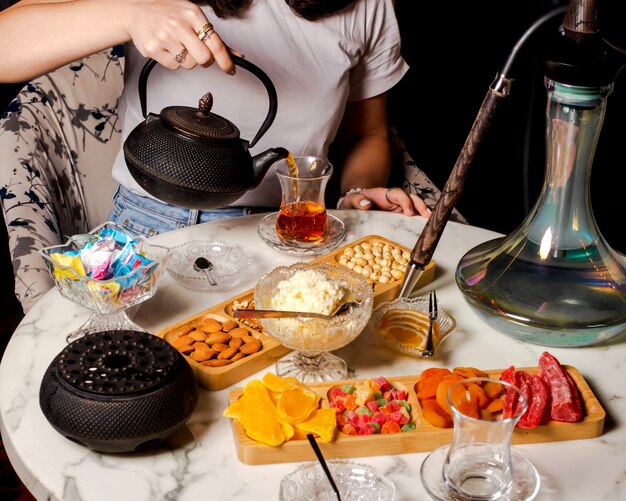 Mujer vertiendo té negro en un vaso con forma de pera servido en la configuración de té