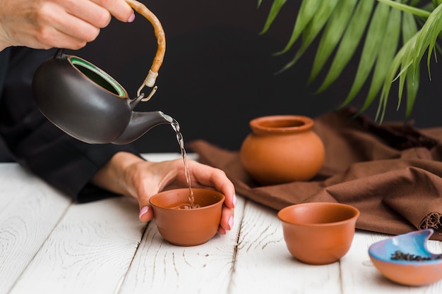 Foto gratuita mujer vertiendo té en taza de arcilla