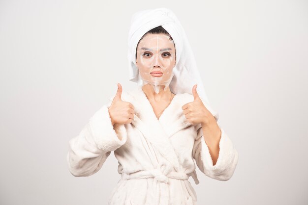 Mujer vestida con albornoz y toalla con mascarilla.