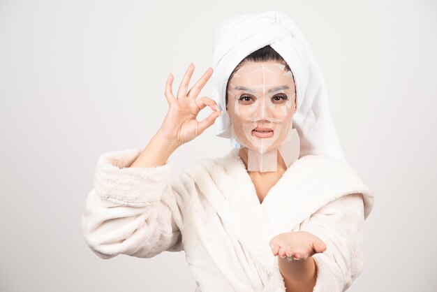 Mujer vestida con albornoz y toalla con mascarilla.