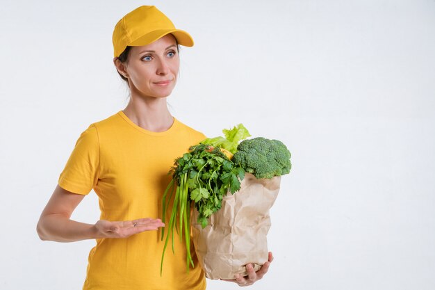 Una mujer vestida de amarillo, entregando un paquete de comida, sobre un fondo blanco.