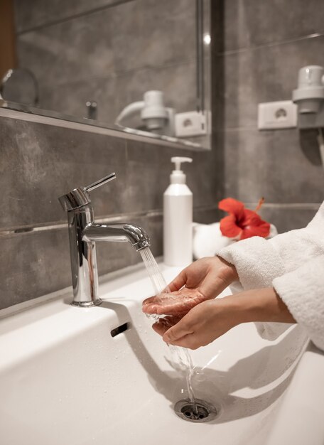 Una mujer vestida con una bata se lava las manos con agua corriente de un grifo.