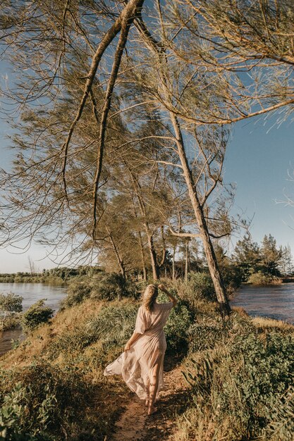 Mujer vestida de blanco caminando descalzo en una pequeña zona cubierta de hierba rodeada de agua