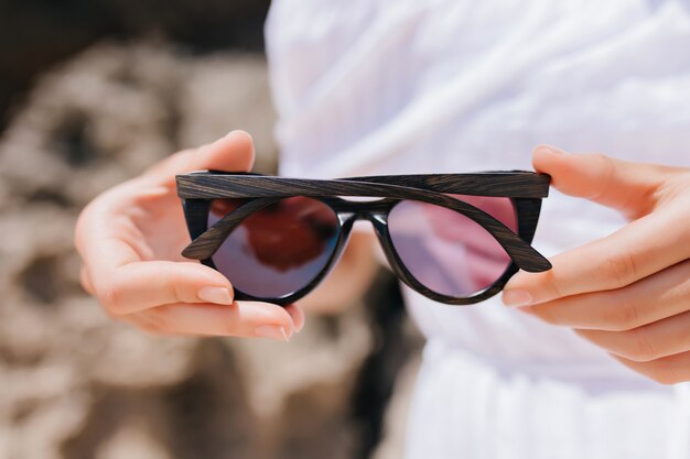 Mujer vestida de blanco con gafas oscuras. Foto de manos femeninas con gafas de sol.