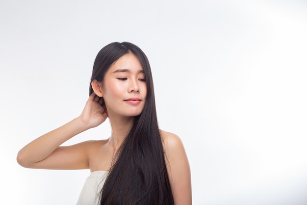 La mujer, vestida con blusas blancas sin tirantes y manos, toca su cabello.