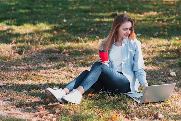 Mujer vestida casual que trabaja en la computadora portátil en la naturaleza