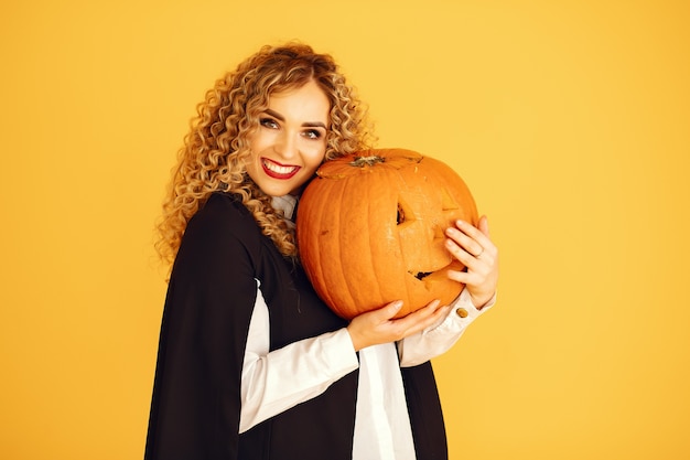 Mujer vestida con traje negro. Señora con maquillaje de halloween. Chica de pie sobre un fondo amarillo.