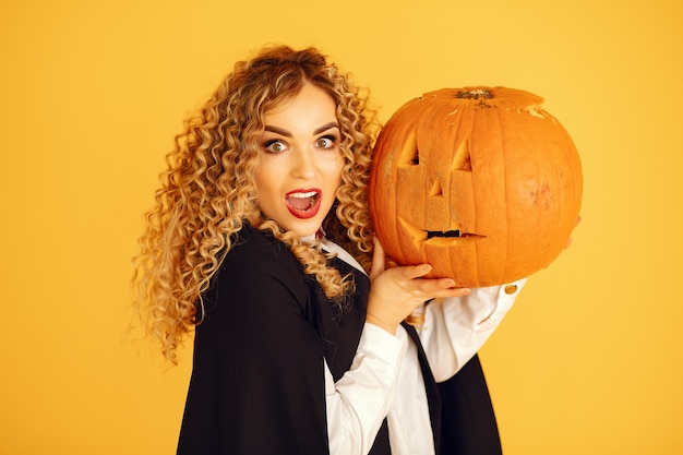 Mujer vestida con traje negro. Señora con maquillaje de halloween. Chica de pie sobre un fondo amarillo.