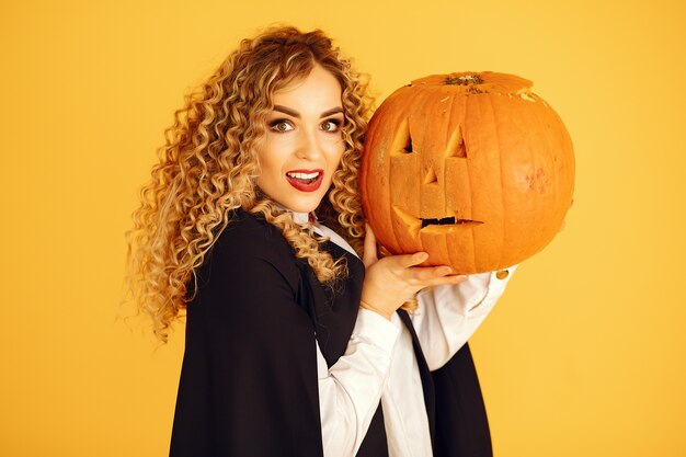 Mujer vestida con traje negro. Señora con maquillaje de halloween. Chica de pie sobre un fondo amarillo.