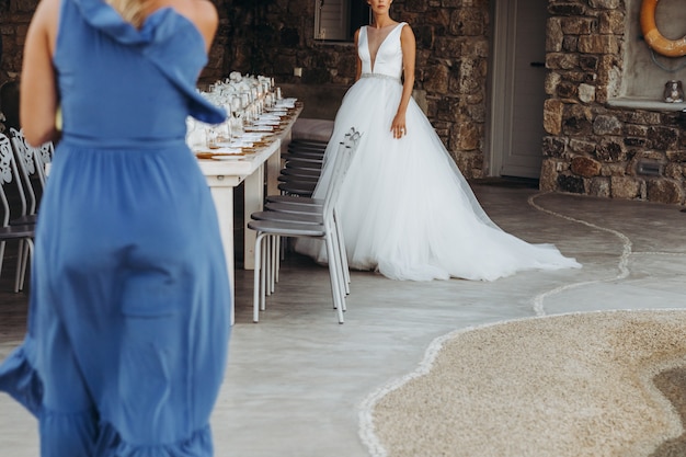 Mujer con vestido azul camina hacia la novia en elegante vestido de novia