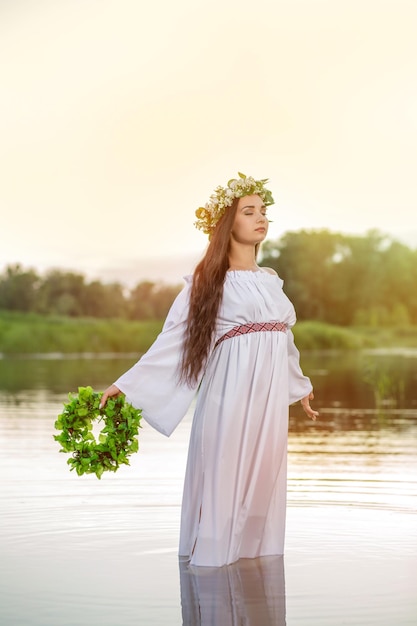 Mujer con vestido blanco en el agua. Arte Mujer con corona en la cabeza en el río. Chica bruja mojada en el lago, misteriosa mujer mística. Corona en la cabeza, tradiciones eslavas y paganismo.