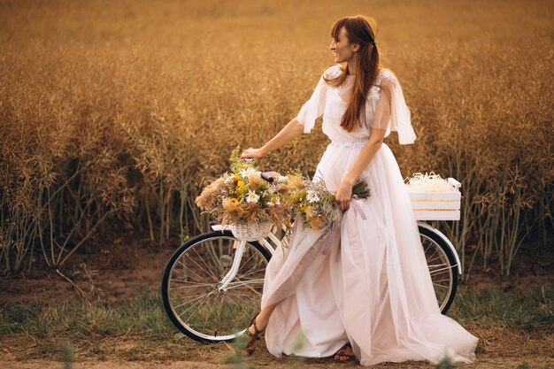 Mujer en vestido blanco con bicicleta en el campo