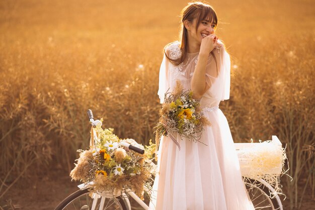 Mujer en vestido blanco con bicicleta en el campo