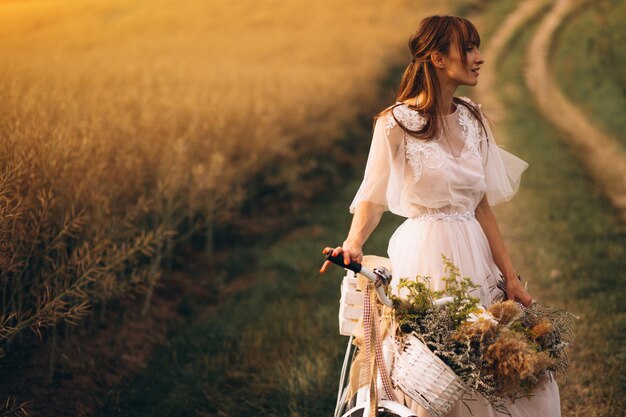 Mujer en vestido blanco con bicicleta en el campo