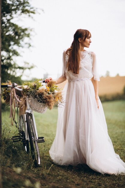 Mujer en vestido blanco con bicicleta en el campo