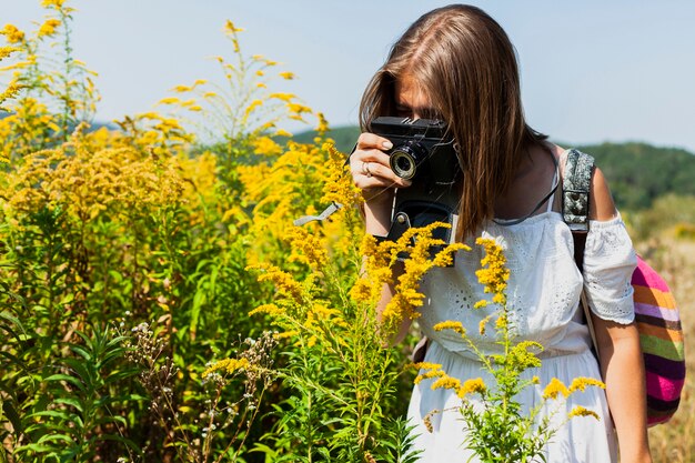 Mujer con vestido blanco tomando fotos de flores amarillas