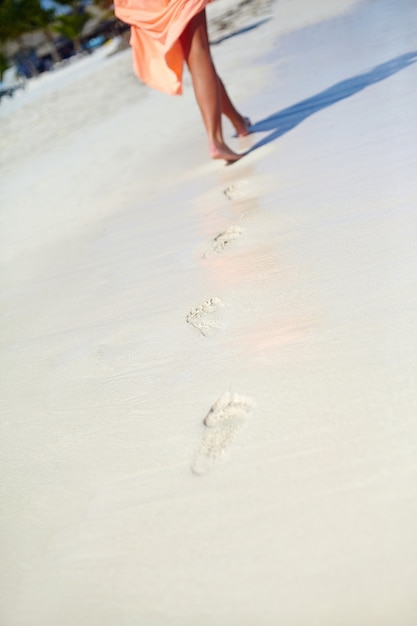 Mujer en vestido colorido caminando en la playa del océano dejando huellas en la arena