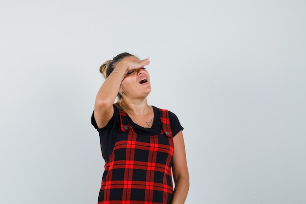 Mujer en vestido delantal sosteniendo la mano en los ojos y mirando pacífica, vista frontal.