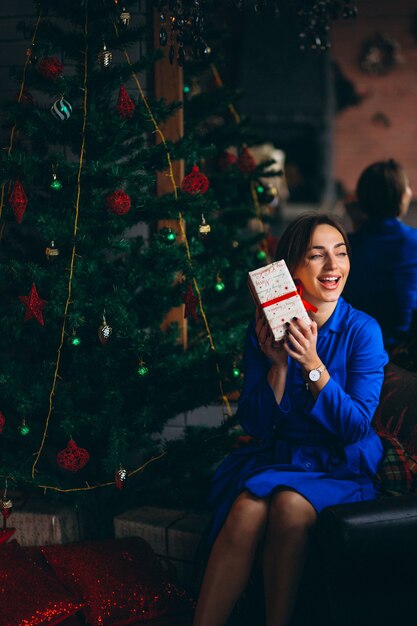 Mujer en vestido hermoso sentado por el árbol de navidad