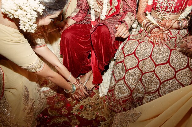 La mujer en el vestido indio beige dobla a los pies de los pares de la boda