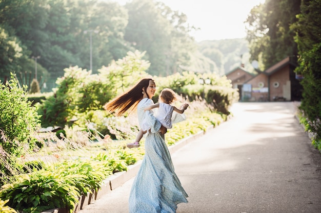 Mujer en vestido largo azul gira con su pequeña hija en la ruta del pavimento