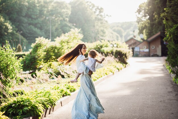 Mujer en vestido largo azul gira con su pequeña hija en la ruta del pavimento