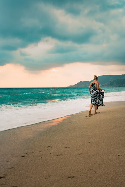 Mujer en vestido largo caminando por la orilla del mar