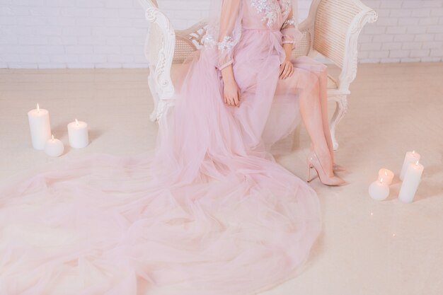 Mujer en vestido largo rosa se sienta en una silla rodeada de velas brillantes