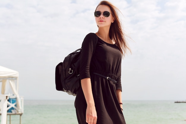 Mujer con vestido negro y gafas de sol en la playa