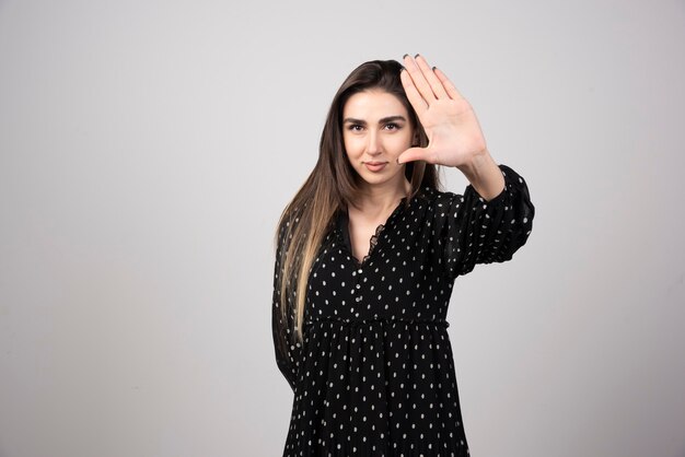 Mujer en vestido negro haciendo señal de stop en gris.