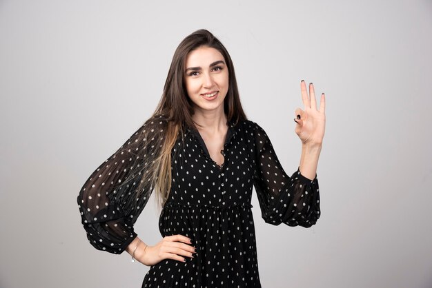 Mujer en vestido negro mostrando signo ok en gris.