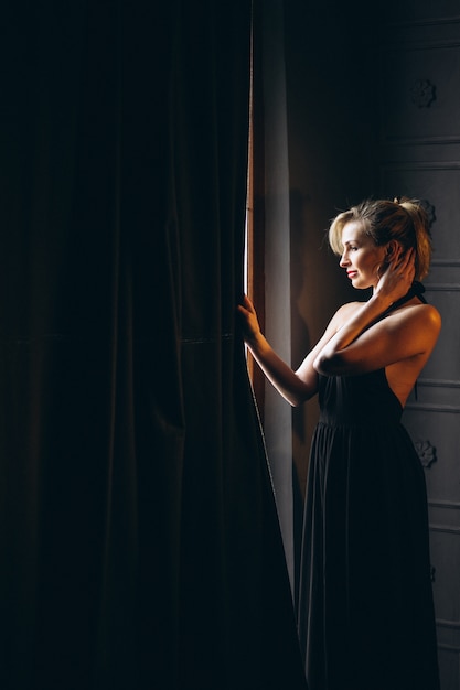 Mujer en vestido negro de pie junto a la ventana