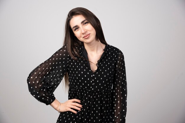 Mujer en vestido negro de pie sobre gris.