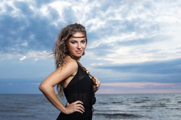 Mujer en vestido negro posando a la orilla del mar