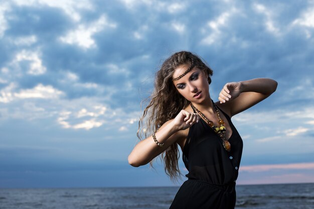 Mujer en vestido negro posando a la orilla del mar