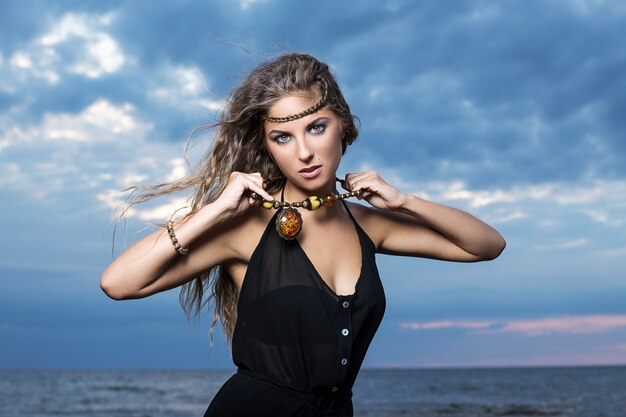 Mujer en vestido negro posando a la orilla del mar