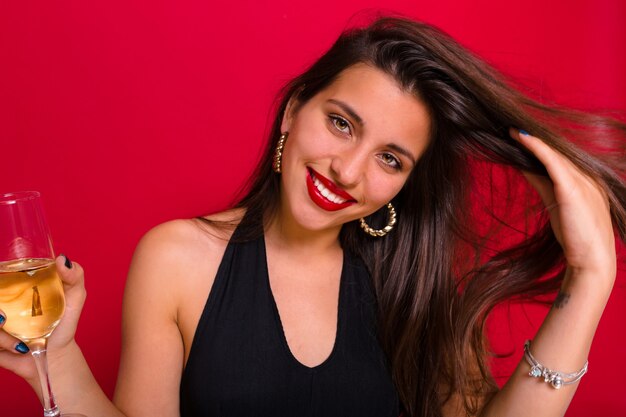 mujer con un vestido negro y sosteniendo una copa de champán posando en rojo