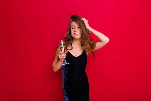 mujer con un vestido negro y sosteniendo una copa de champán posando en rojo