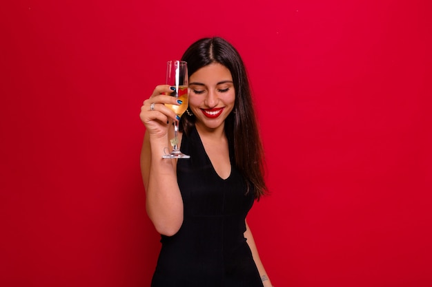 mujer con un vestido negro y sosteniendo una copa de champán posando en rojo