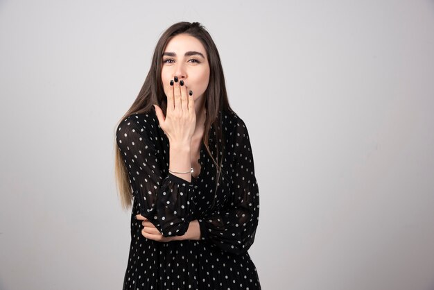 Mujer en vestido negro tapándose la boca en gris.