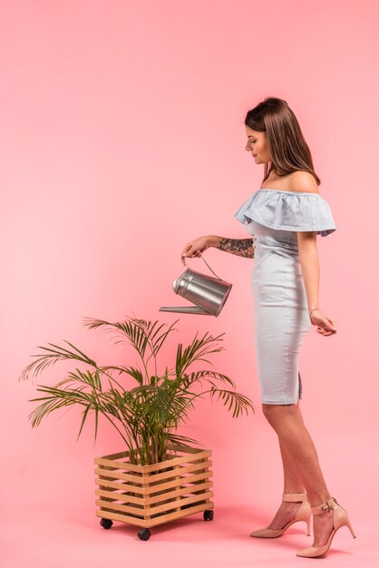 Mujer en vestido regando planta verde en maceta