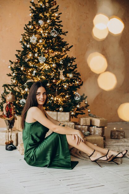 Mujer en vestido verde hermoso sentado junto al árbol de Navidad