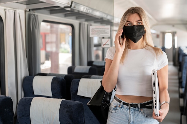 Mujer viajando en tren y hablando por teléfono mientras usa máscara médica