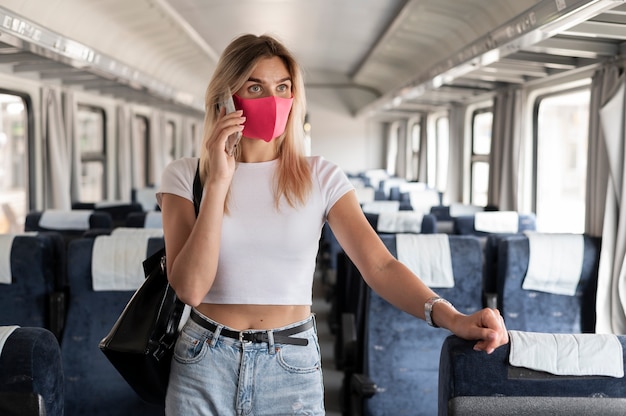 Mujer viajando en tren y hablando por teléfono mientras usa máscara médica