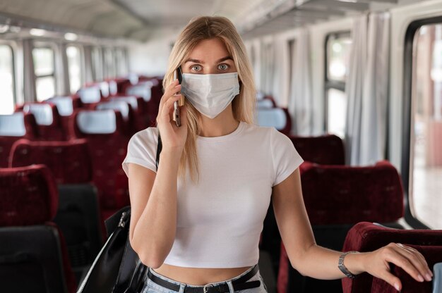 Mujer viajando en tren y hablando por teléfono mientras usa máscara médica