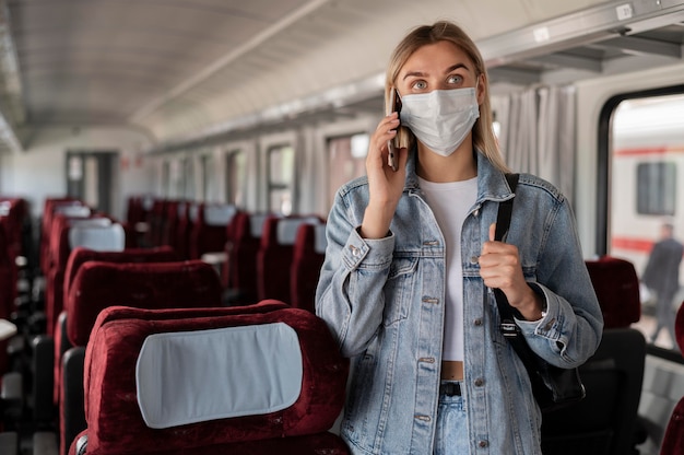 Mujer viajando en tren y hablando por teléfono mientras usa máscara médica