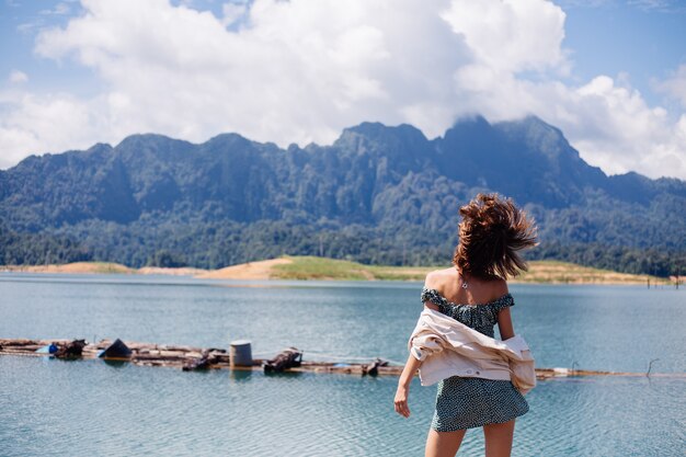 Mujer en viaje turístico de vestido y chaqueta de verano en Tailandia, parque nacional de Khao Sok, vista increíble en barcos y lago.