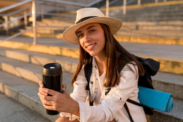 Mujer viajera con mochila y sombrero sosteniendo termo