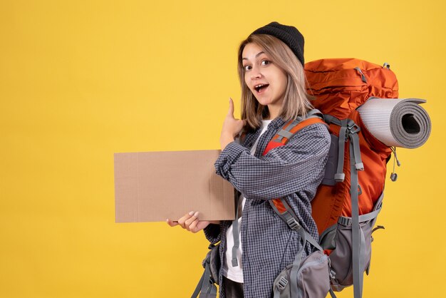 Mujer viajera con mochila sosteniendo cartón apuntando hacia atrás